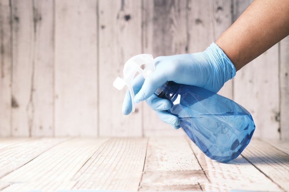 Gloved hand holding a disinfectant spray bottle